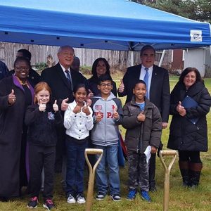 elected leaders and young kids under a blue tend with their thumbs up, gold shovels in front of them in the ground